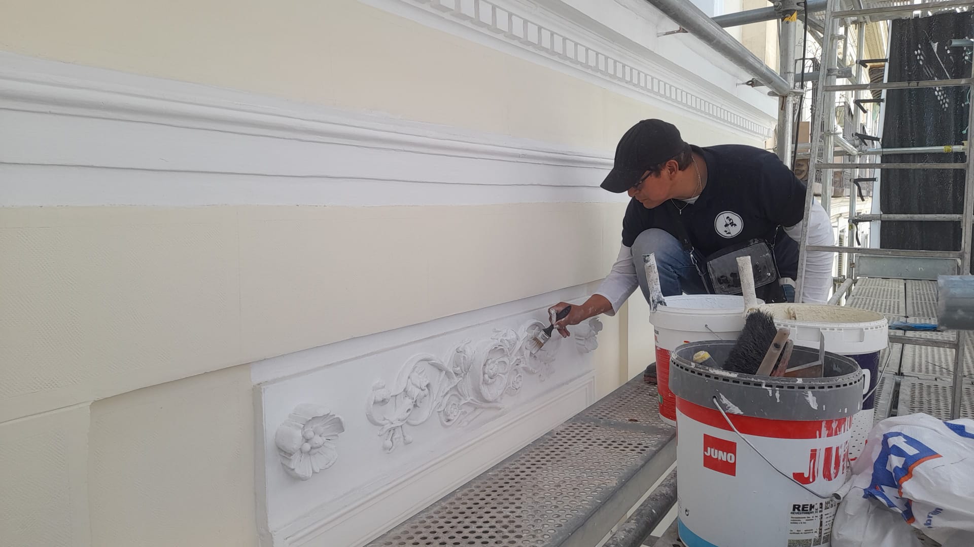 Operario pintando una moldura decorativa desde un andamio.
