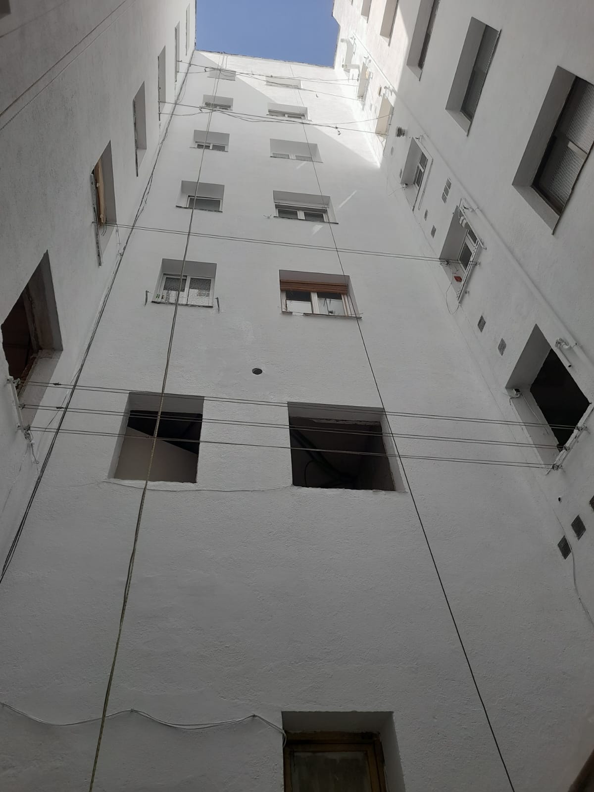 Paredes blancas de un patio interior con ventanas y cuerdas de trabajo.