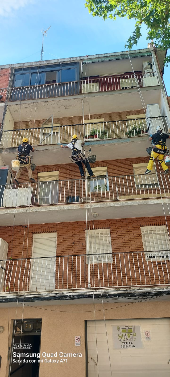 Tres operarios trabajando con cuerdas en la fachada de un edificio